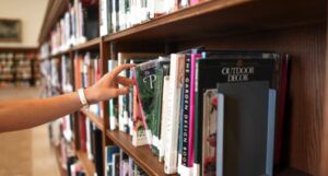 beige colored arm and hand reaching for a library book on a shelf