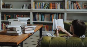 image of a woman reading a book on a green couch and a pile of books on a brown wooden desk https://www.pexels.com/photo/girl-reading-book-on-brown-wooden-table-4861353/