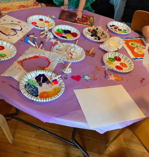 image of table with paints, plates, and kid's paintings